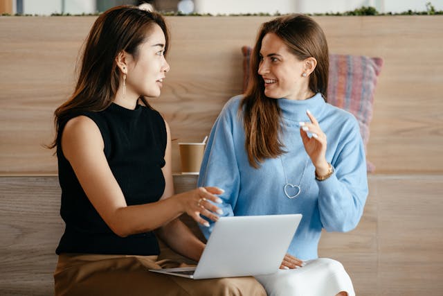 Foto de um duas mulhere sentadas. Uma delas está com um notebook no colo explicando coisa para a outra que sorri, como se a tivesse orientando profissionalmente. A foto ilustra o artigo 10 Estratégias para Transformar os seus Padrões de Comportamento escrito pelo psicanalista Homero Mônaco para o site Online Psicanalista.