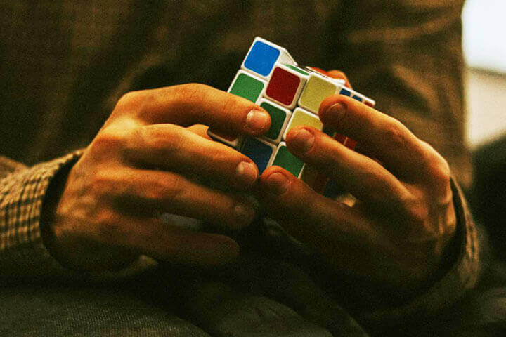 Foto das mãos de um homem sentado, girando um cubo mágico simbolizando a resolução de problemas. A foto ilustra o artigo 10 Técnicas Criativas para o Sucesso na Resolução de Problemas escrito pelo psicanalista Homero Mônaco para o site Online Psicanalista.