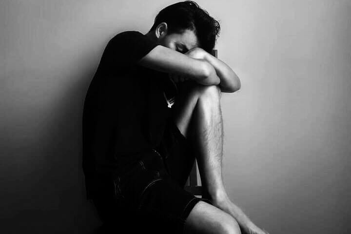 Foto preta e branca de um homem sentado no chão, com um joelho em pé, no qual ele apoia os braços e cabeça. Ele parece estar com depressão. A foto ilustra o artigo Como a Psicanálise trata a depressão escrito no blog do psicanalista Homero Mônaco para o site A Sessão de Terapia.