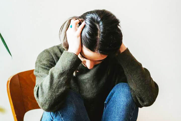 Foto de uma mulher sentada em uma cadeira de madeira, no consultório de seu psicanalista, com as mãos no ouvido e cabeça como se estivesse com crise de estresse, ansiedade ou depressão. A foto ilustra o artigo O Papel da Terapia Psicanalítica no combate à Ansiedade, ao Estresse e à Depressão escrito pelo psicanalista Homero Mônaco para o site Online Psicanalista.