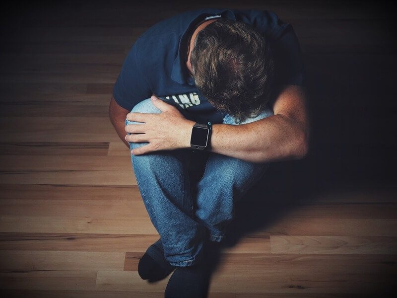 Foto de um homem sentaado em um piso de madeira, encolhido, como se estivesse com depressão/deprimido.A foto ilustra o artigo O que é Depressão? Sintomas, Causas e Tratamentos escrito pelo psicanalista Homero Mônaco para o site Online Psicanalista.