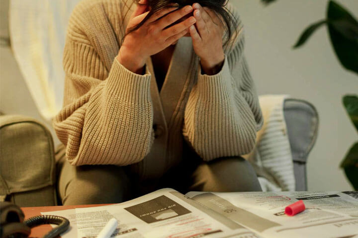 Foto de uma mulher com mão no rosto, e cabeça abaixada, debruçada em um jornal como se estivesse preocupada com a sua busca de emprego. A foto ilustra o artigo Os Impactos Causados pela Inteligência Artificial: Social, Comportamental, Psicológico e Cognitivo escrito pelo psicanalista Homero Mônaco para o site Online Psicanalista.