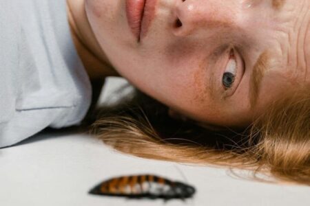 Foto do rosto de uma mulher ruiva deitada no chão com uma cara de assustada pois está com fobia de ver uma barata passando bem próximo ao seu rosto. A foto ilustra a página do Perfil do Psicanalista Homero Mônaco para o site A Sessão de Terapia.