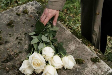 Foto da mão direita de um homem deixando um maço de rosas brancas em cima de um túmulo pois está de luto e triste por sua perda. A foto ilustra a página do Perfil do Psicanalista Homero Mônaco para o site A Sessão de Terapia.