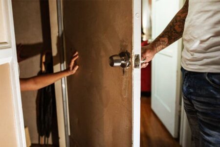 Foto de um homem abrindo uma porta que ele arrombou, e é possível ver o braço de uma pessoa tentando impedi-lo para evitar sofrer um trauma. A foto ilustra a página do Perfil do Psicanalista Homero Mônaco para o site A Sessão de Terapia.